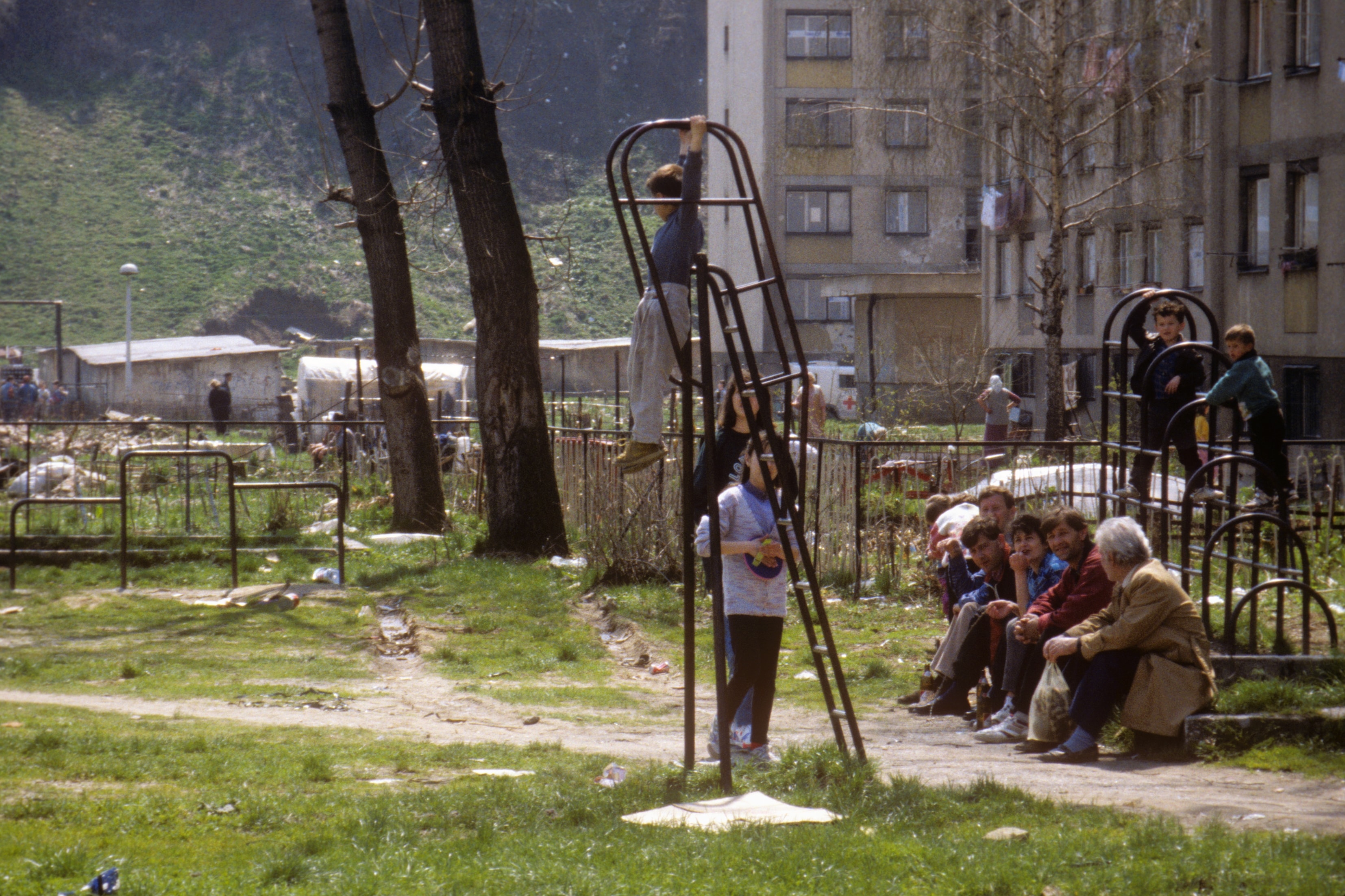 Children playing on a playground with a refugee camp in the background in Bosnia