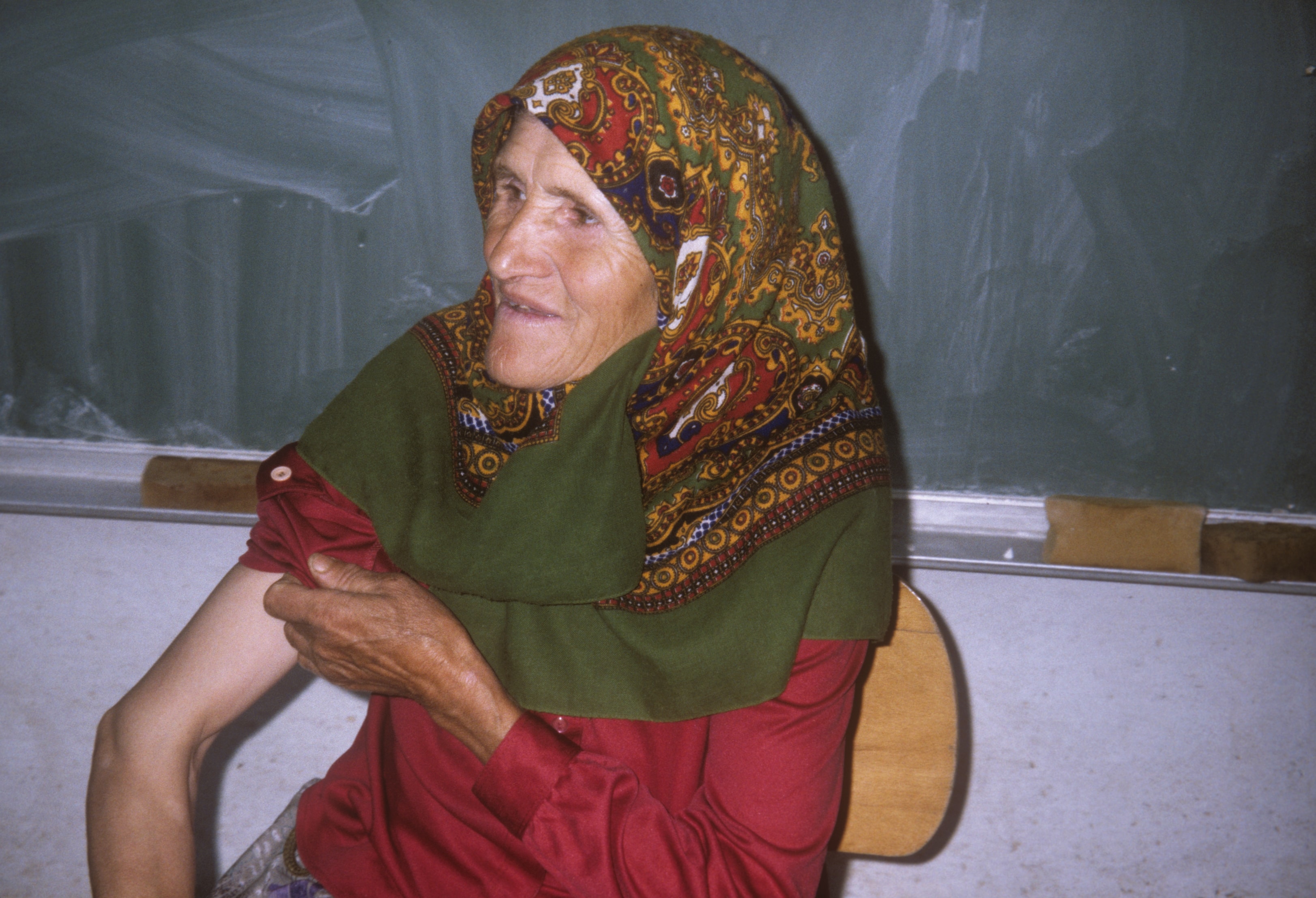 Elderly Bosnian woman in colorful headscarf seated in a classroom