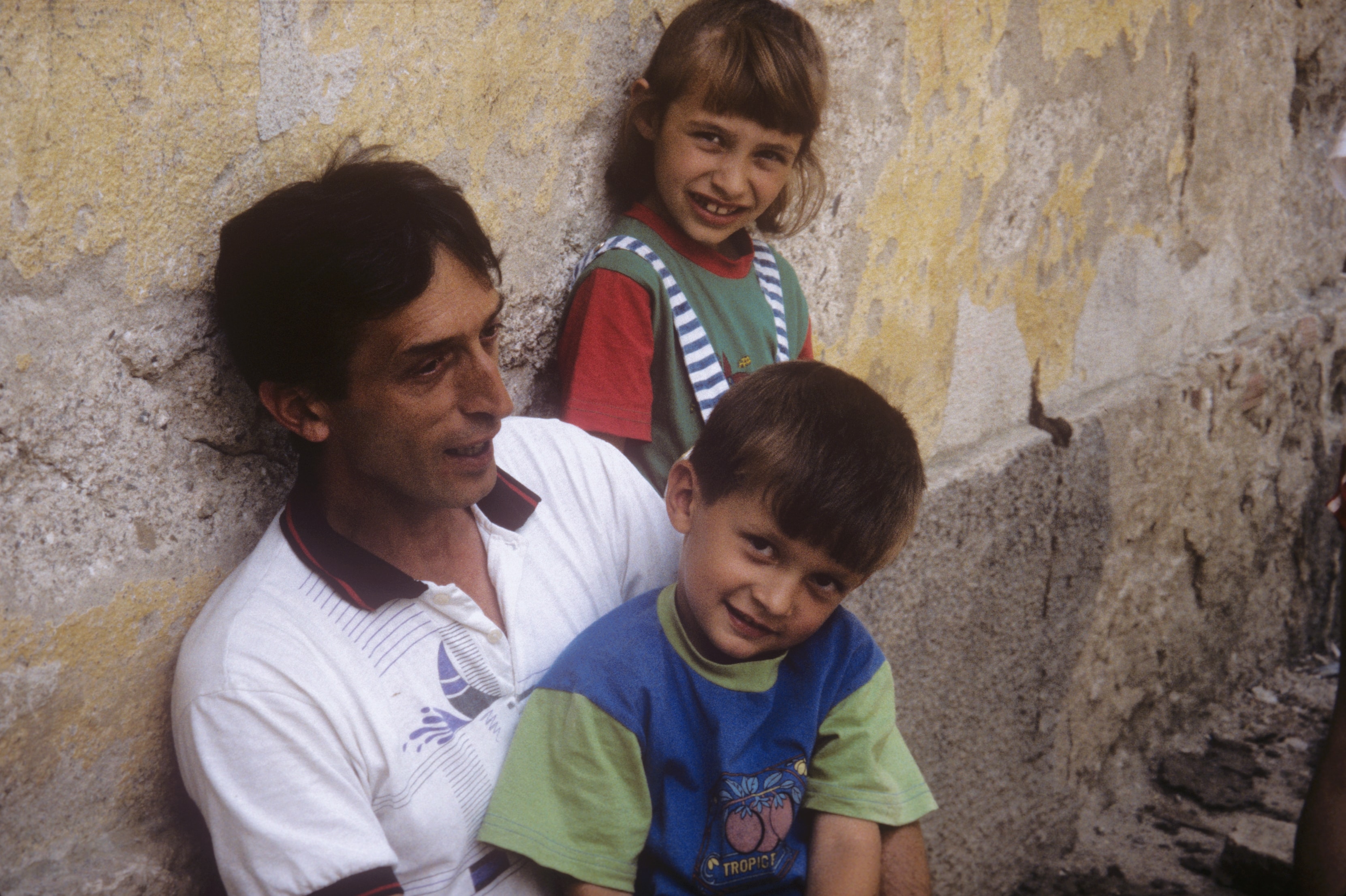 Father with two young children against a weathered wall in Bosnia