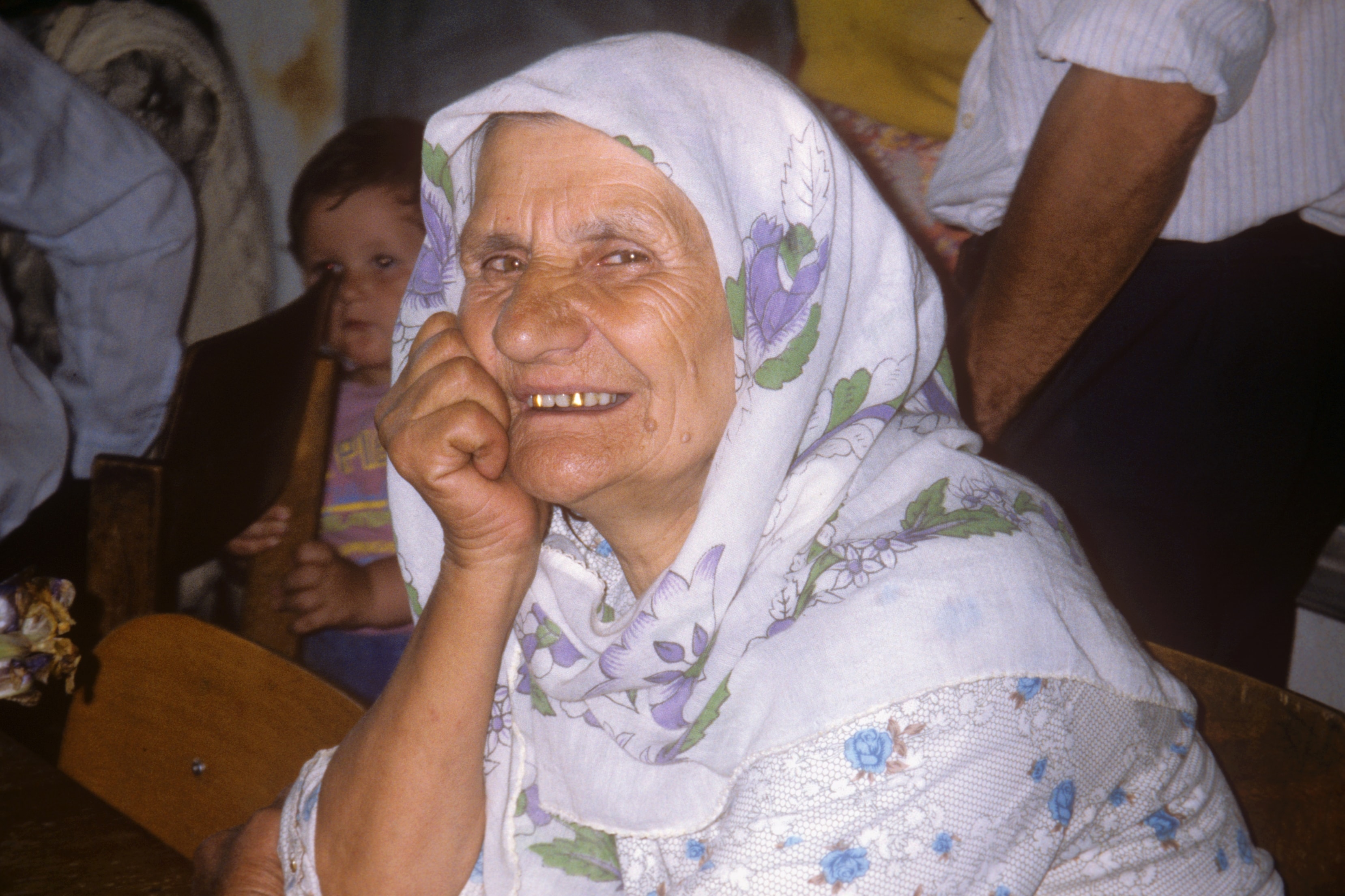 Smiling Bosnian woman in a floral headscarf with a child behind her