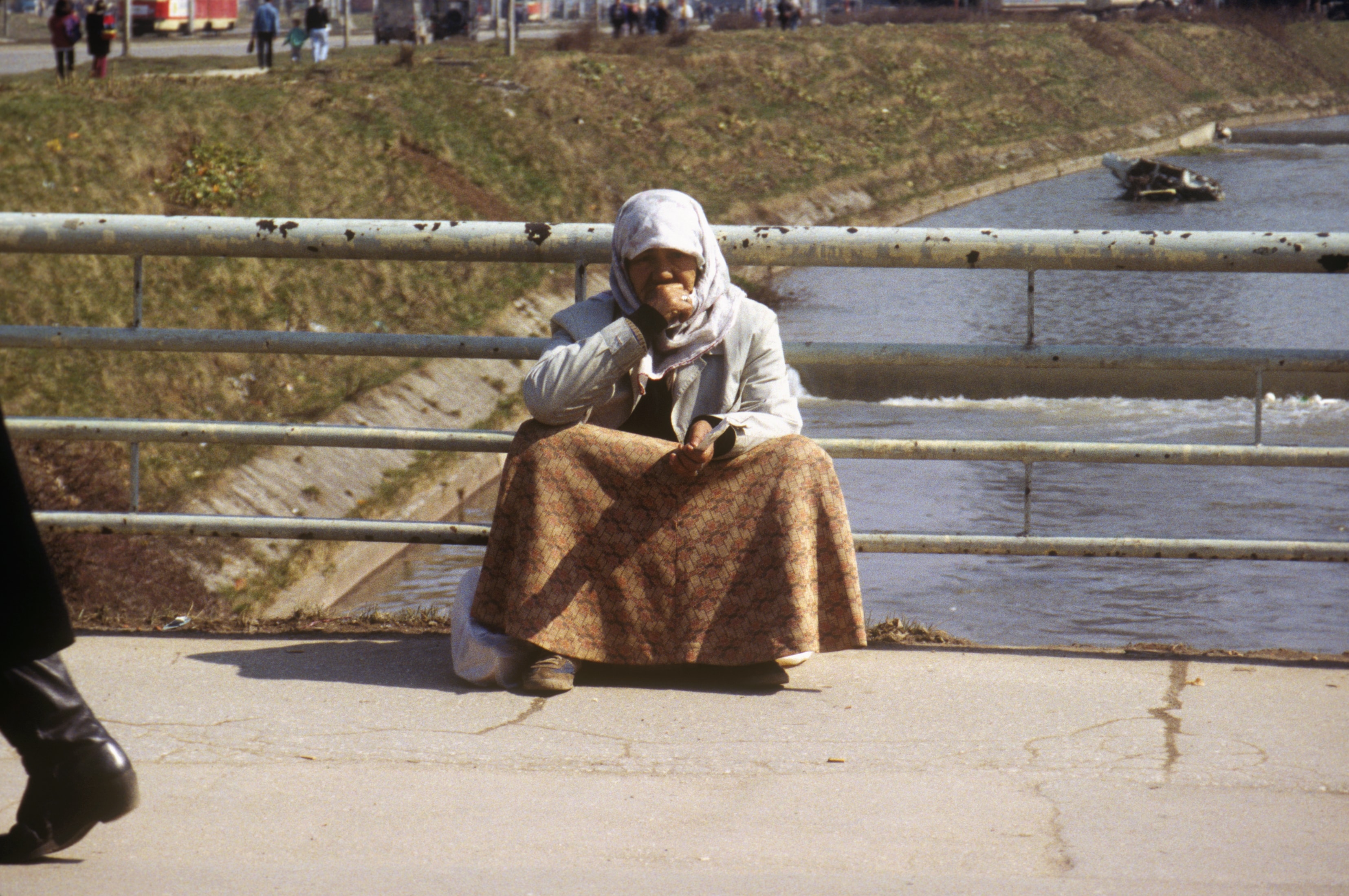 Elderly woman sitting on a bridge over a river in Bosnia