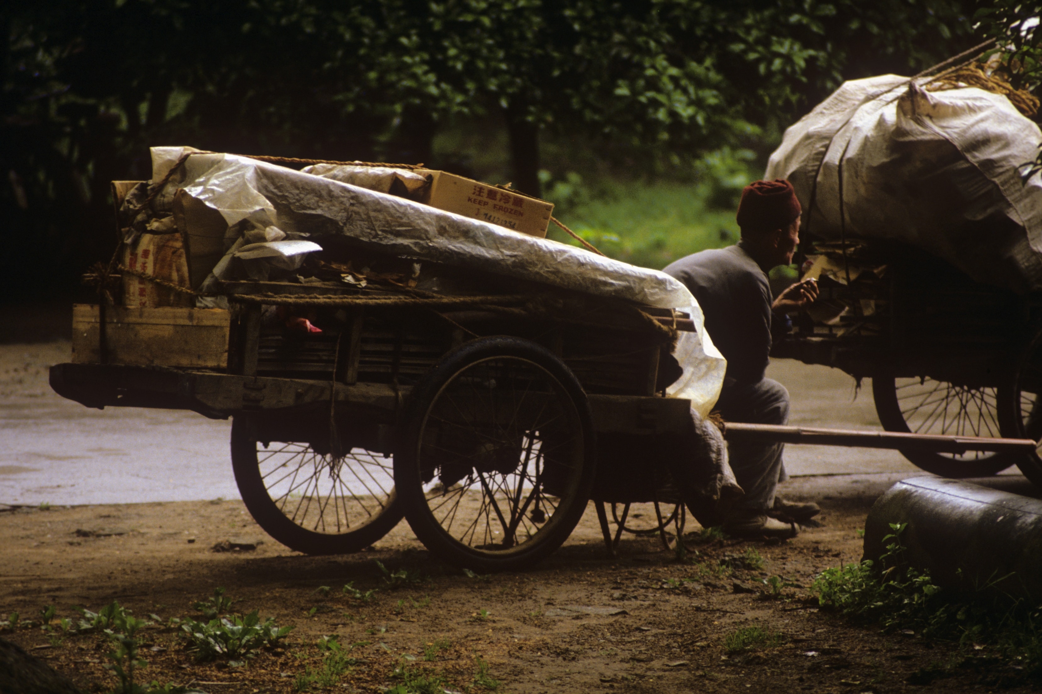 Worker resting beside loaded hand-pull cart, China