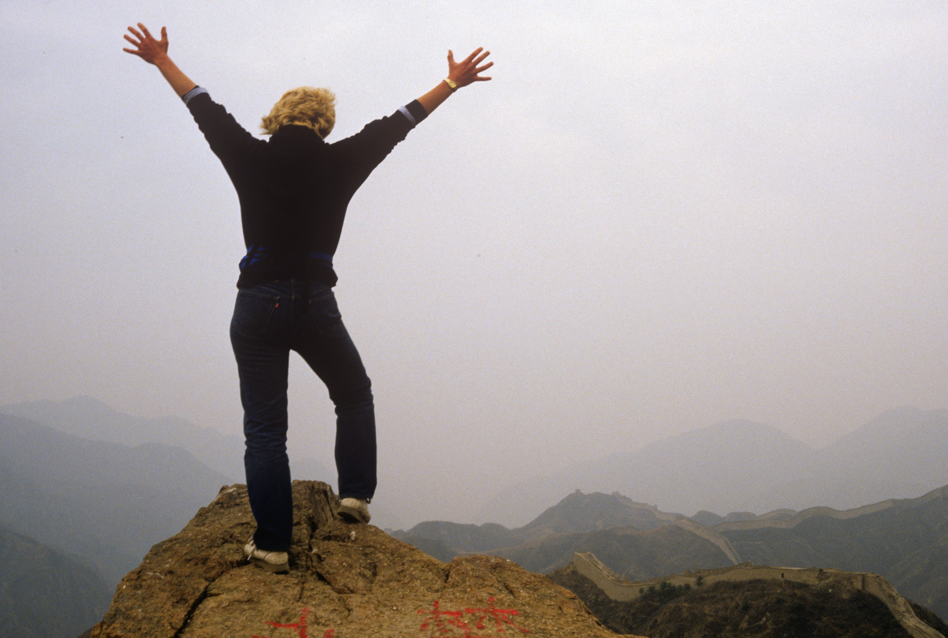 Susan celebrating on mountain summit above Great Wall