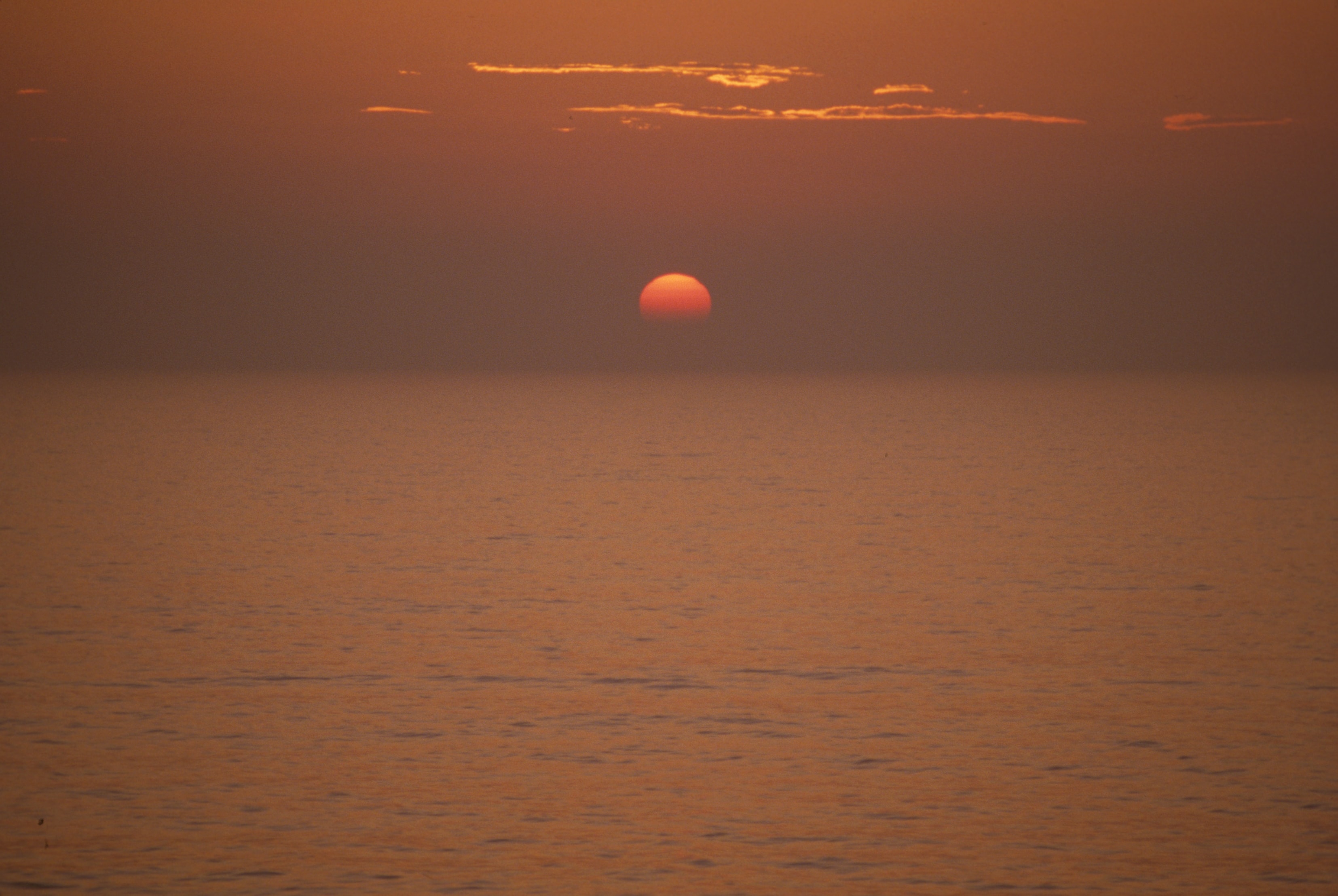 Glowing red sun setting over calm ocean, China
