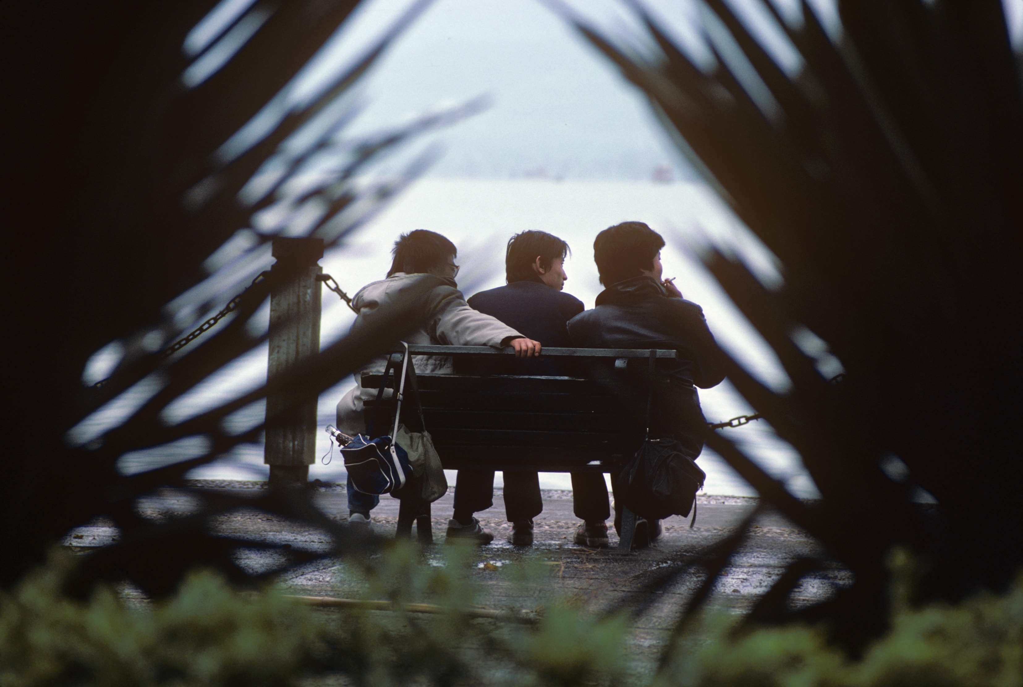 Three people sitting on bench framed by lattice, China