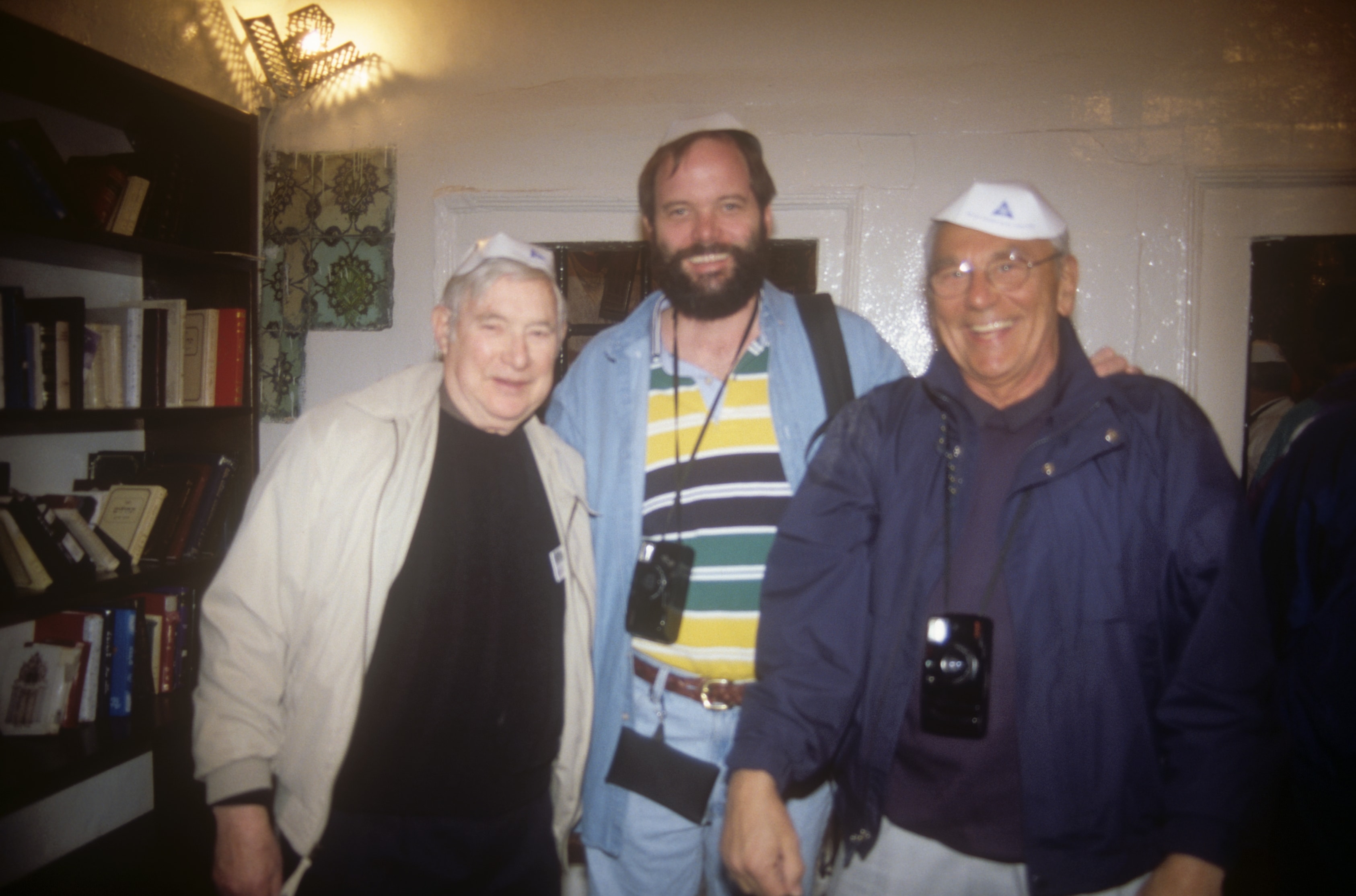 Three men smiling together indoors wearing tour caps in the Holy Land