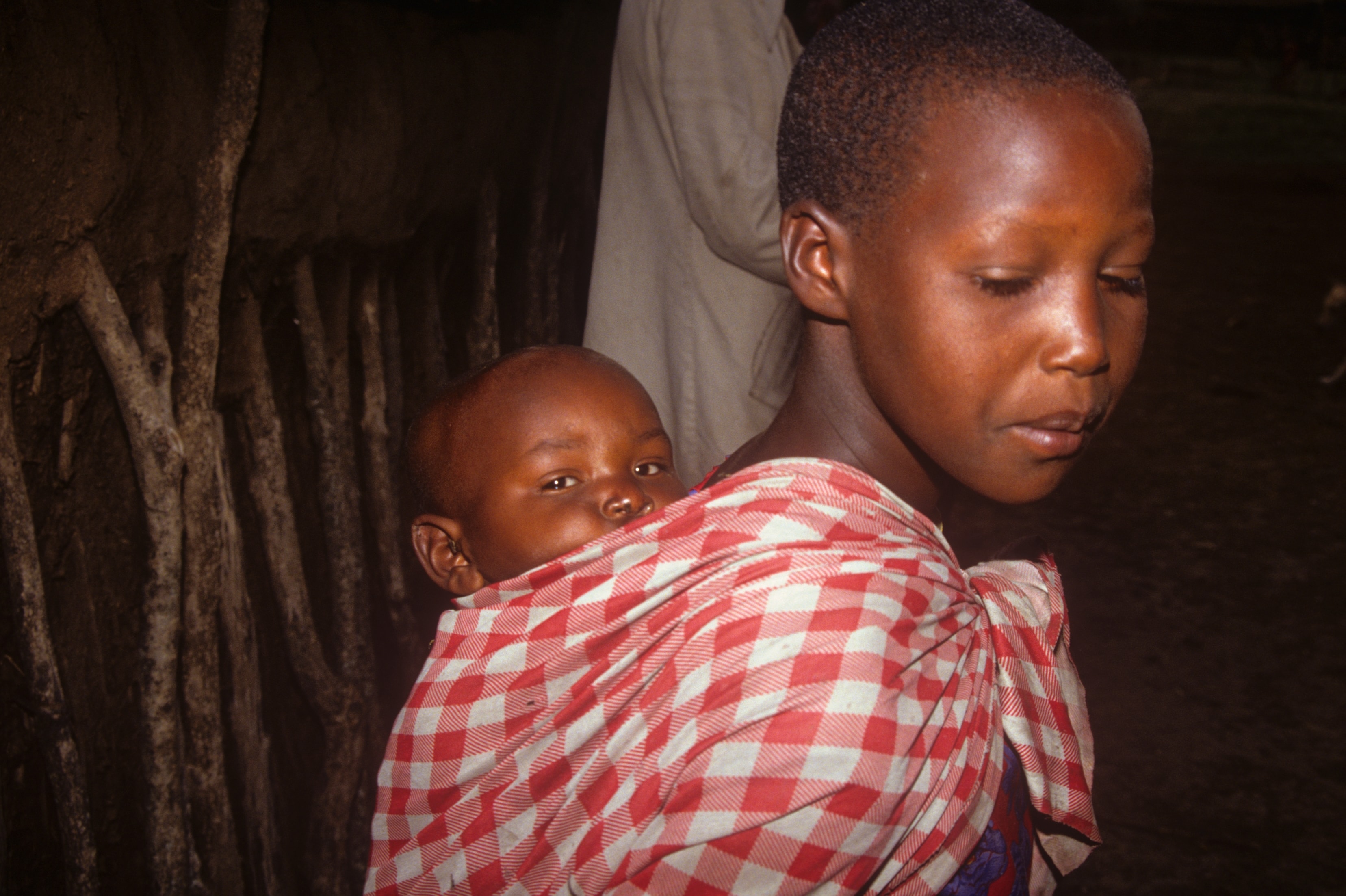 Mother carrying her baby wrapped in a red and white cloth in Kenya