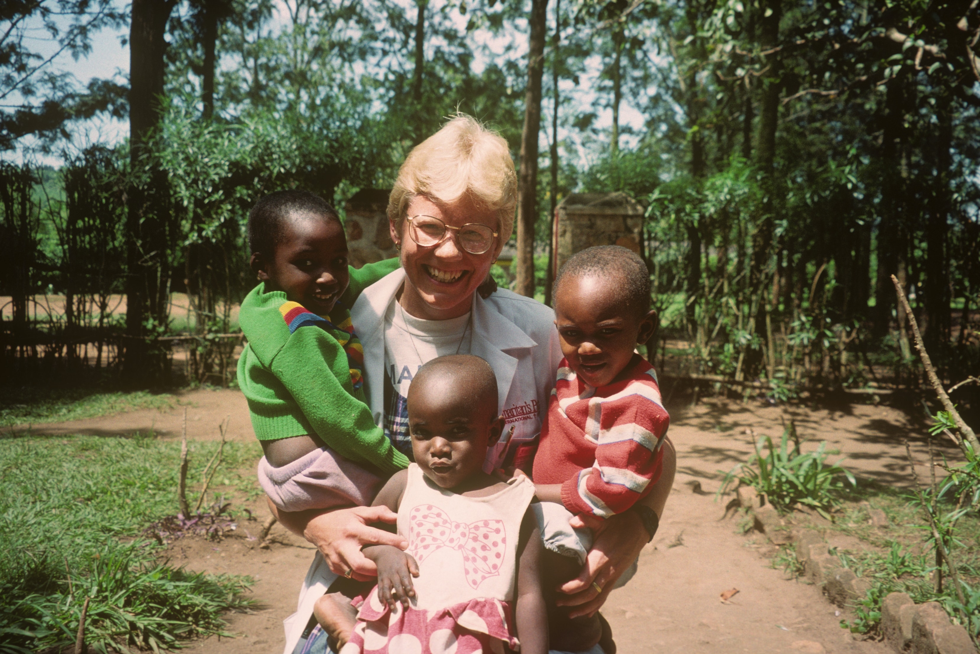 Dr. Susan Vitalis laughing while holding three young children outdoors in Rwanda