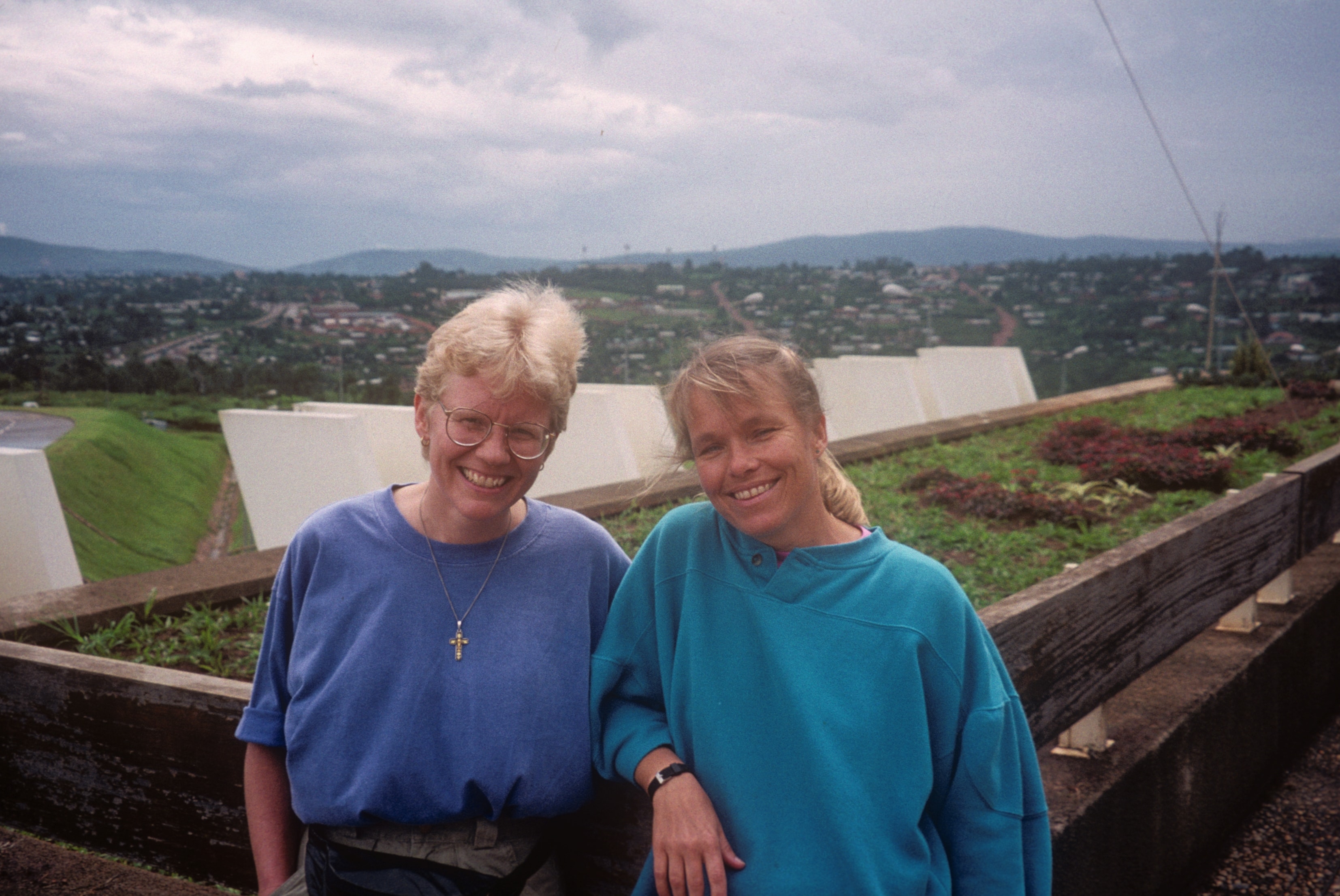 Two women smiling together with a city and green hills in the background in Rwanda