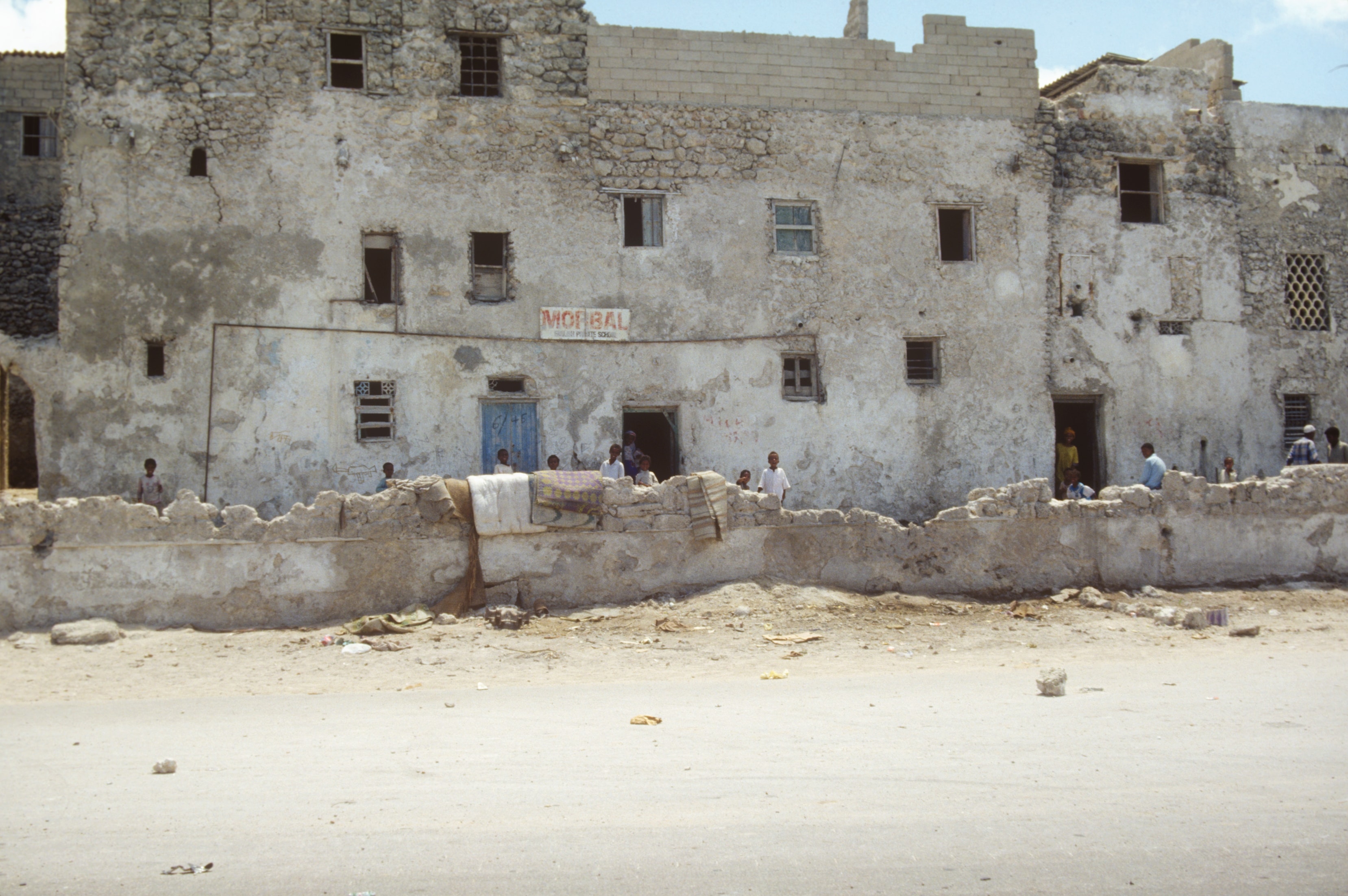 Weathered multi-story building with children gathered outside on a dusty street in Somalia