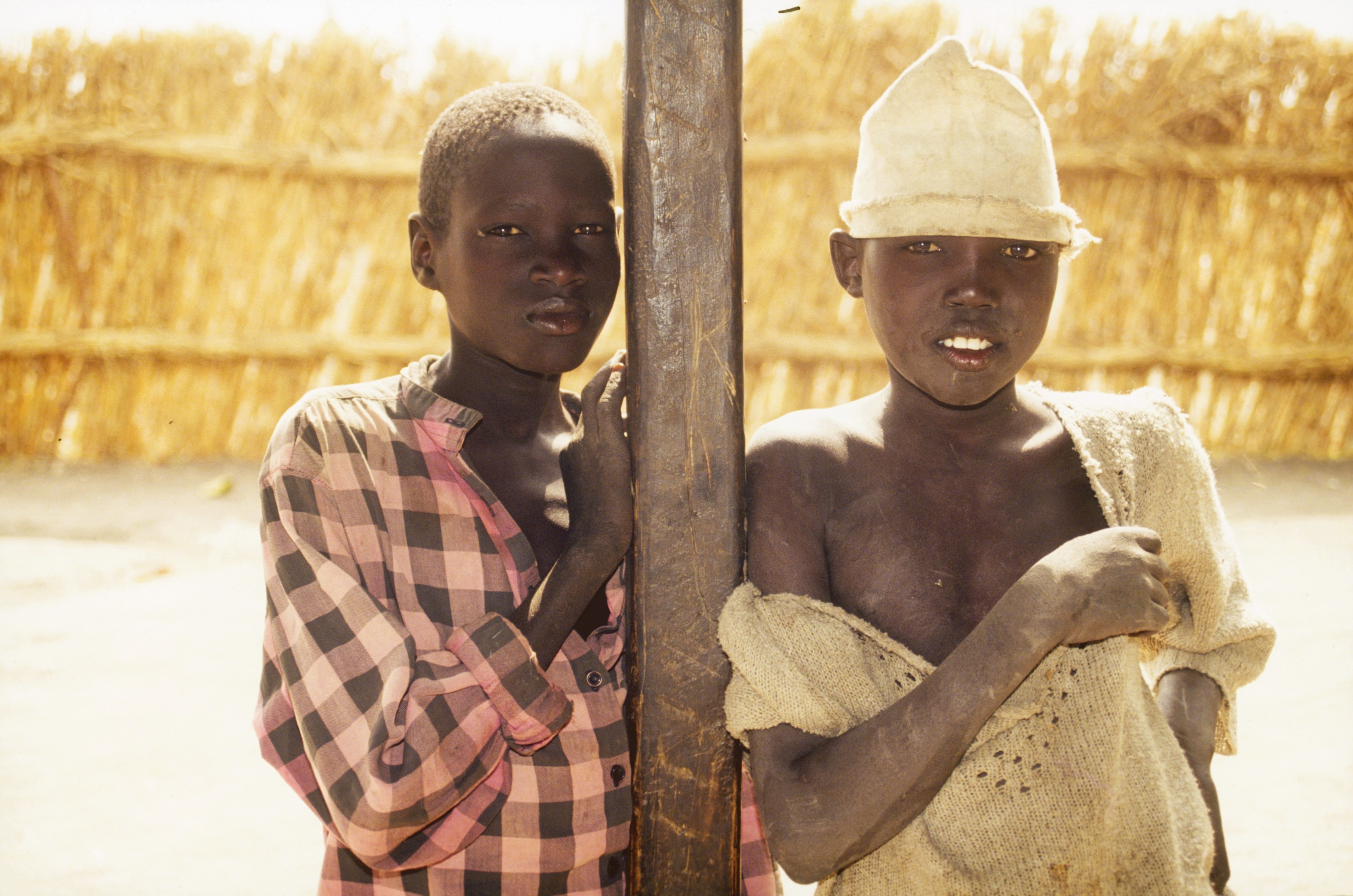 Two boys standing by a wooden post in an arid village in Sudan