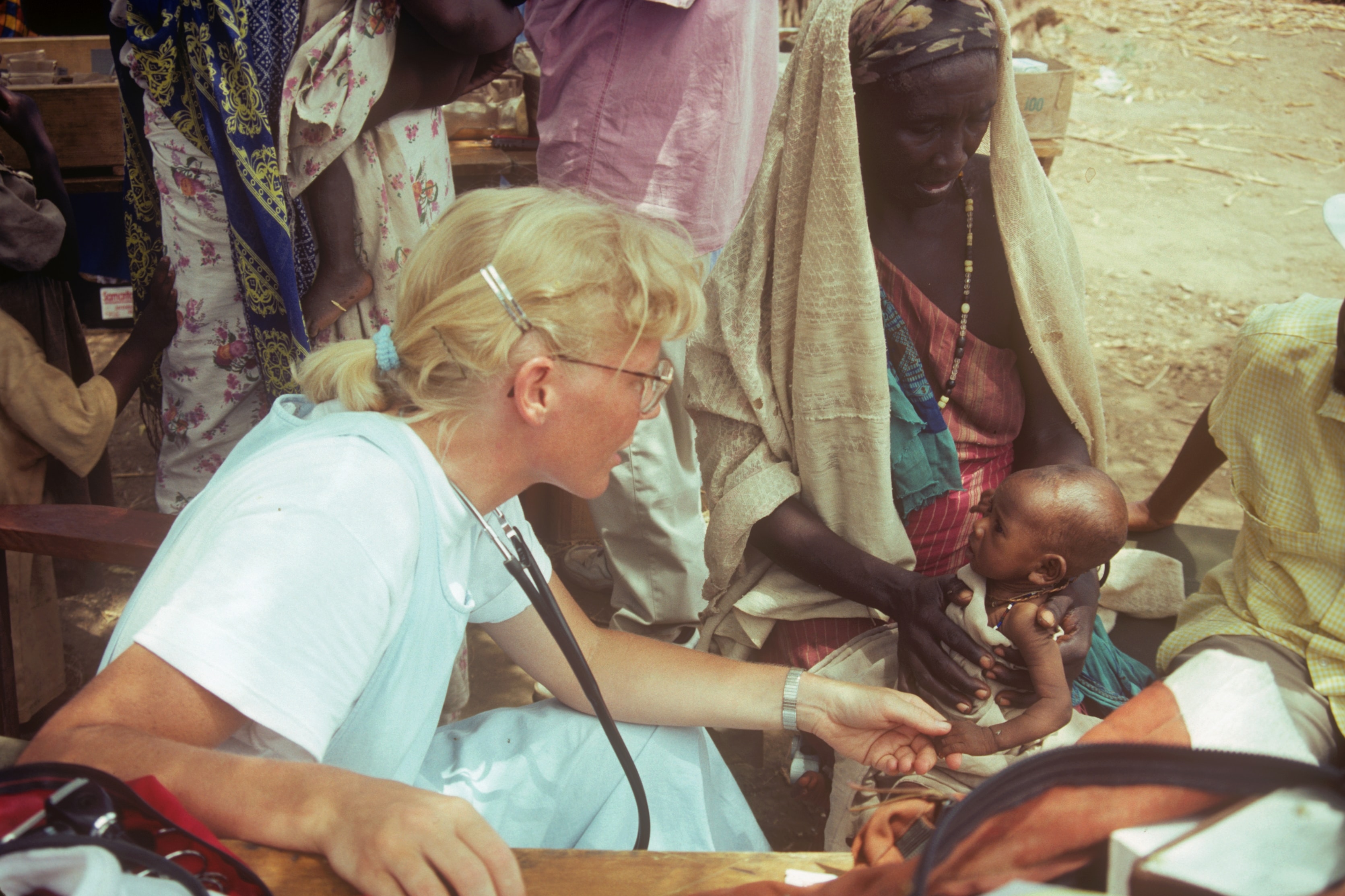 Dr. Susan Vitalis examining a baby held by its mother at an outdoor clinic in Sudan