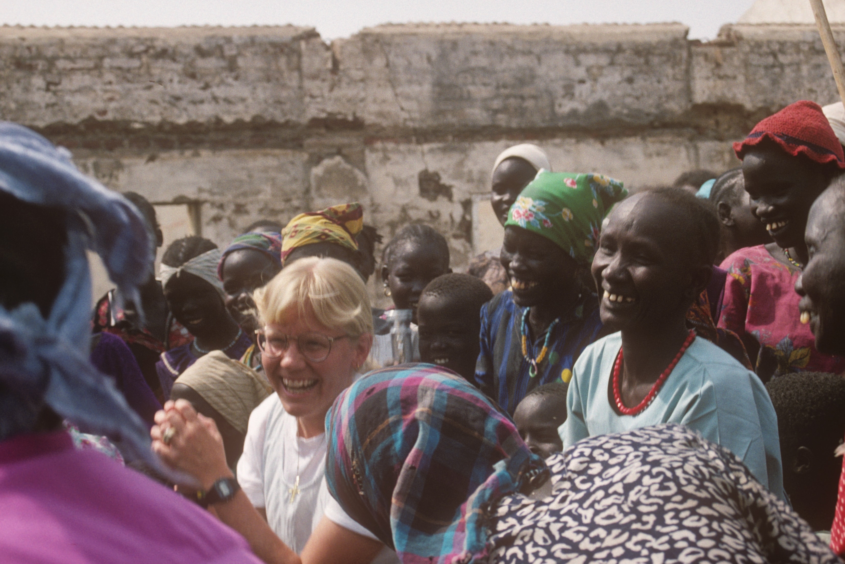 Dr. Susan Vitalis laughing joyfully among a group of Sudanese women outdoors
