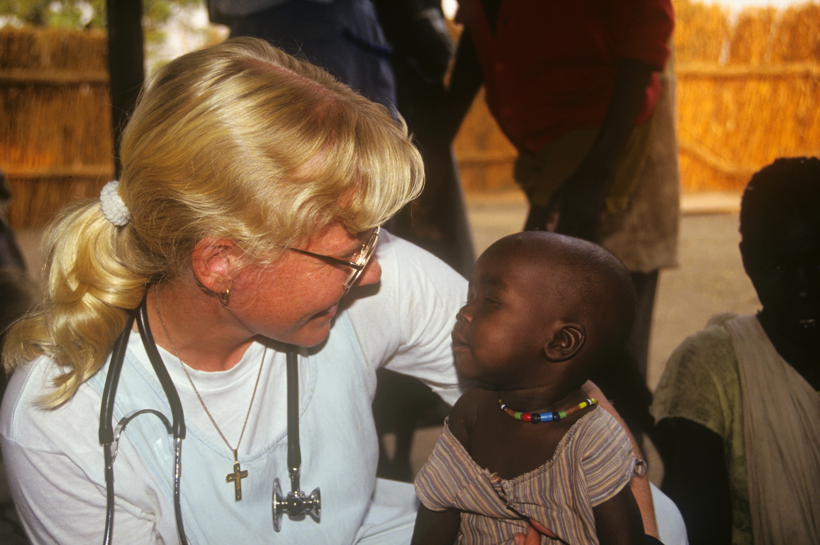Dr. Susan Vitalis with stethoscope looking closely at a young child in Sudan