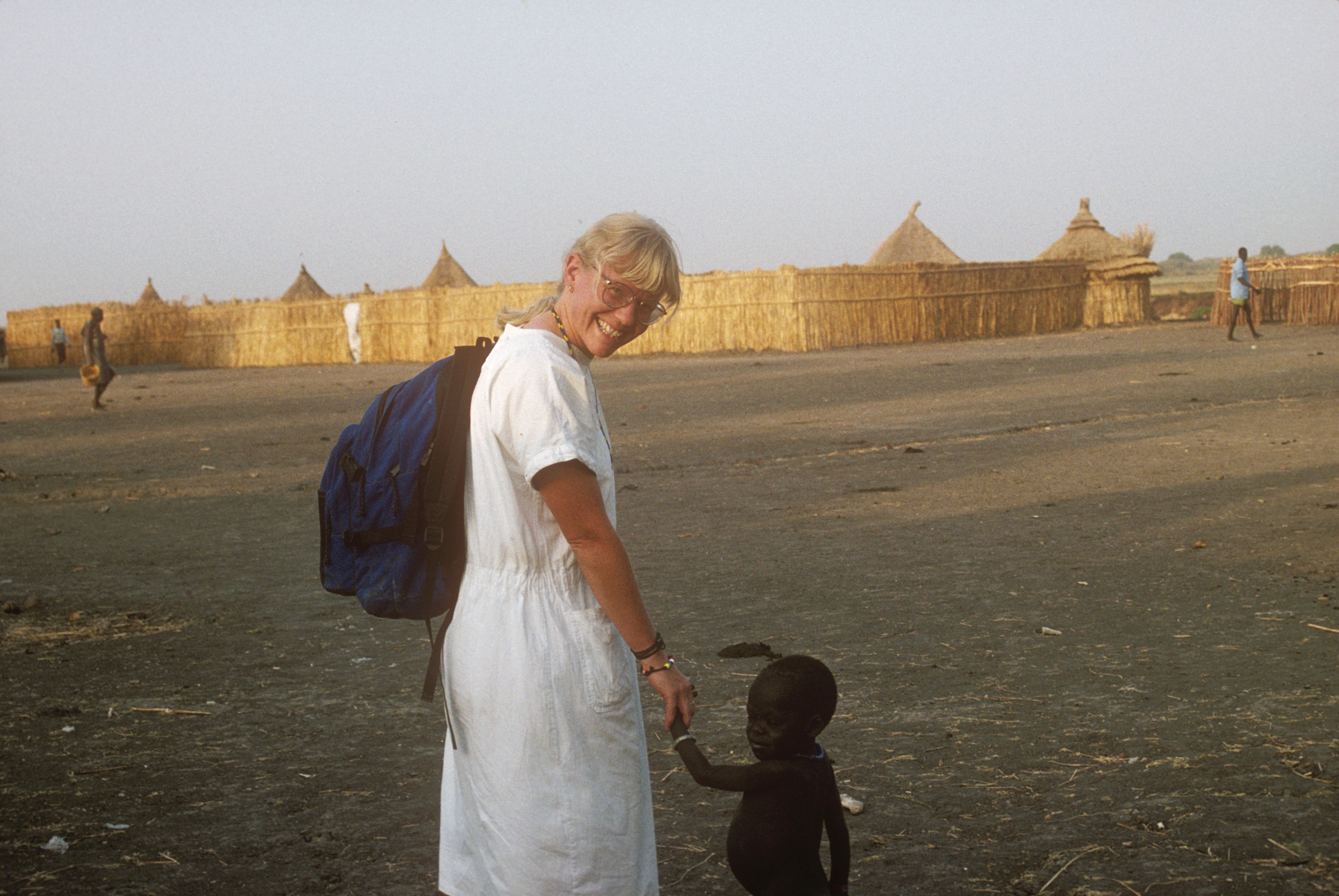 Dr. Susan Vitalis walking hand-in-hand with a small child in a Sudanese village